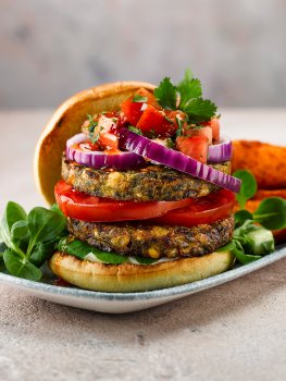 Close up food photograph of a vegetarian burger with two patties, sliced tomato, sliced red onion, tomato salsa, lambs lettuce and sweet potato fries