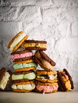 Food photograph of a stack of ice cream sandwiches, various flavours of ice cream each sandwiched between two cookies, some using chocolate chip cookies and some with double chocolate cookies