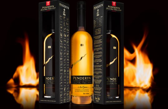 Drinks photograph of a special edition Welsh whisky celebrating Wales' six nations Grand Slam victory in 2019, two bottles of whisky in commemorative boxes either side of a bottle of whisky out of its box, presented on a reflective black background with flames behind