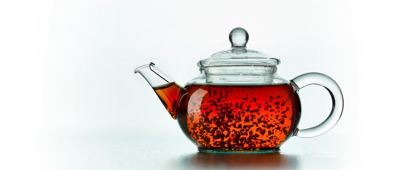 Drinks photograph close up of an individual serving glass teapot filled with loose leaf tea infusing and swirling around the teapot, shot isolated on a reflective white background