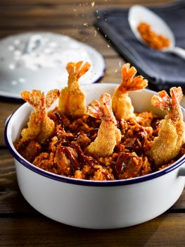 Food photograph of battered shrimp jambalaya, large deep fried battered prawns in a jambalya of pork and rice served in an enamel pot on a wooden background