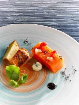 Food photograph closeup of a fine dining starter, salmon mi-cuit served with a miniature brioche roll, horseradish cream, grapefruit pearls, squid ink sauce and nasturtium leaves