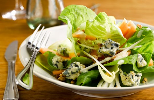 Food photograph close up of a roquefort and melon salad, juicy ripe canteloupe melon and crumbled roquefort cheese, served on a salad of lettuce and chicory. Shot in a restaurant setting alongside a glass of white wine and a glass bottle of table water