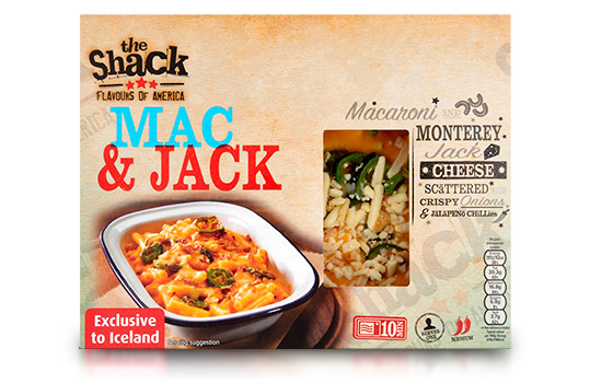 Food photograph of a front of pack image for The Shack Mac & Jack frozen ready meal, an enamel dish filled with macaroni in a thick cheese sauce topped with sliced jalapeno, shot on a dark wood setting with ingredients in the background, and the front of pack itself shown over the photograph
