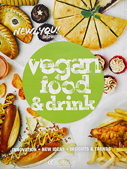 Photograph of two vegan food magazine covers, and a spread from inside a vegan food magazine, featuring a variety of food photographs of vegan dishes including hot dogs, tacos, mock duck pancakes, fish and chips and a cauloflower curry
