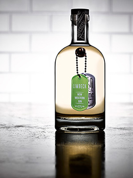 Drinks photograph of four bottles of small batch gin, each shown individually on a reflective metal tabletop with white subway tiles in the background
