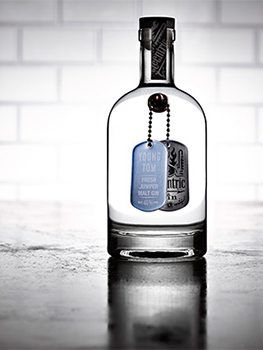 Drinks photograph of four bottles of small batch gin, each shown individually on a reflective metal tabletop with white subway tiles in the background