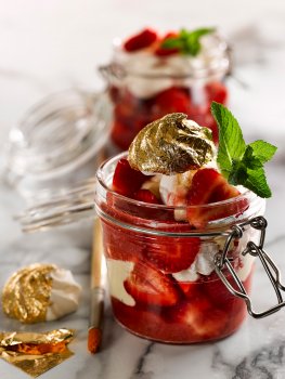 Food photograph of an Eton mess served in a glass kilner jar with fresh strawberries and whipped cream, with gold leaf covered meringue kisses