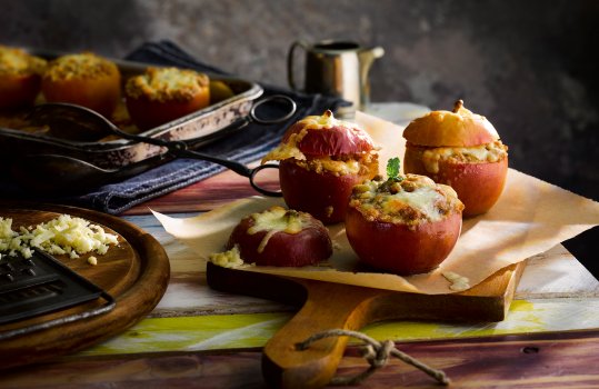 Food photograph close up of three juicy bright red stuffed baked apples topped with Penderyn whisky cheddar cheese