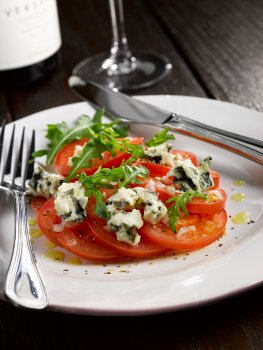Food photograph close up of a fresh tomato, rocket and roquefort cheese salad, shot on a white plate in a restaurant setting