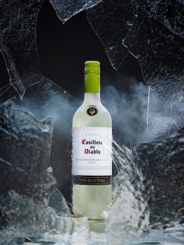 Drinks photograph of a chilled bottle of Casillero Del Diablo 2013 Sauvignon Blanc, shot through several sheets of broken ice on a black background with wisps of smoke