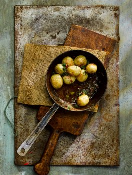 Aerial food photograph close up of a small pan filled with roasted Pembrokeshire Early potatoes, topped with chilli and parsley butter