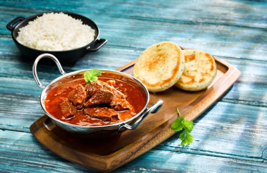 Food photograph close up of a pub style curry, a beef madras served in a silver baltic dish alongside a small ramekin of steamed rice, and miniature naan breads