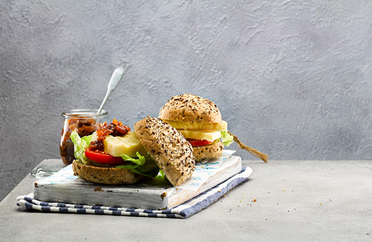Food photograph of a selection of gluten free ploughman’s sandwiches, shot on a grey background on a white chopping board alongside a jar of Welsh chutney