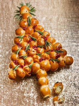 Food photograph of a Christmas rosemary and cranberry tear and share bread, small balls of cranberry bread put together in the shape of a Christmas tree, glazed, baked, and studded with sprigs of rosemary. Served on a gold glitter background