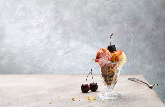 Food photograph of an ice cream sundae featuring scoops of Welsh ice creams in chocolate, strawberry and vanilla flavours, topped with strawberry sauce, chopped nuts and fresh cherries