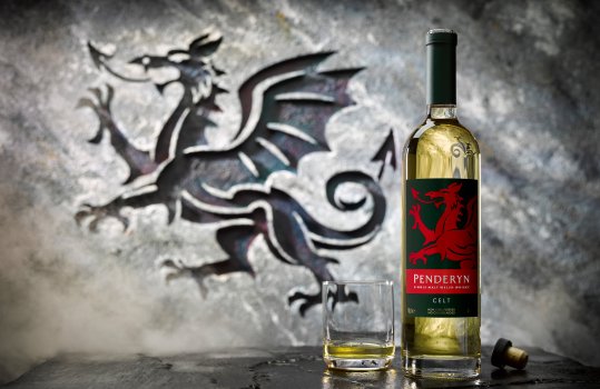 Drinks photograph of a bottle of Penderyn Celt whisky alongside a glass having been poured from the bottle, shot in a medieval looking stone set, with a carving in the stone to mirror the dragon on the label of the bottle