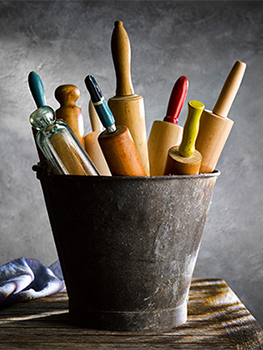 Photograph of a vintage metal pail filled with a selection of vintage rolling pins, shot low key against a dark background