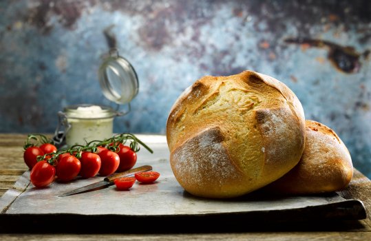 Close up food photograph of two loaves of Pain de Campagne, traditional French style bread shown alongside vine tomatoes and a jar of cream cheese, on a vintage steel tray