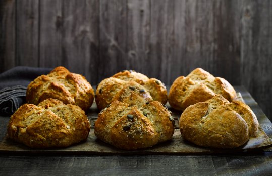 Food photograph of six loaves of homemade traditional soda bread shot lined up on a steel tray, in a dark grey set