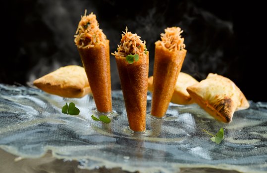 Food photograph of crab cones, a fine dining starter, brick pastry cones filled with picked crab, served stuck in an isomalt sheet on a black background with clouds of smoke