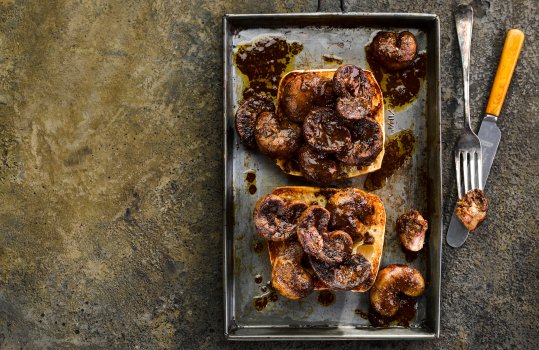 Aerial food photograph of devilled kidneys on toast, fried devilled lamb kidneys served on top of crisp golden sourdough toast; presented on a vintage baking tray on a concrete background