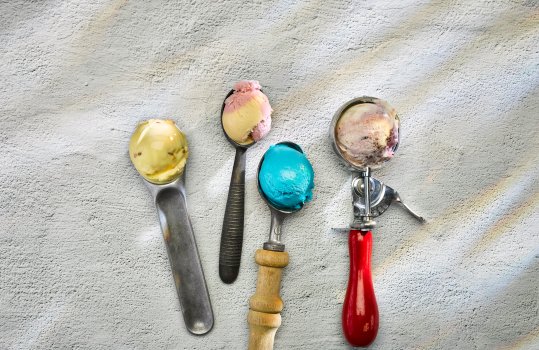 Food photograph of four scoops of ice cream in various flavours on four different vintage ice cream scoops, on a grey stone background