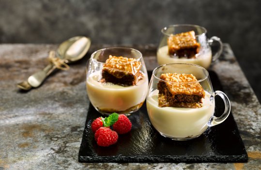 Food photograph close up of sticky toffee pudding slices stacked up in glass teacups filled with custard