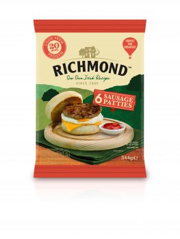 Food photograph of a chopping board with a sausage patty, cheese and egg English muffin, with a ramekin of tomato sauce, on the front of a pack of Richmond Sausage patties